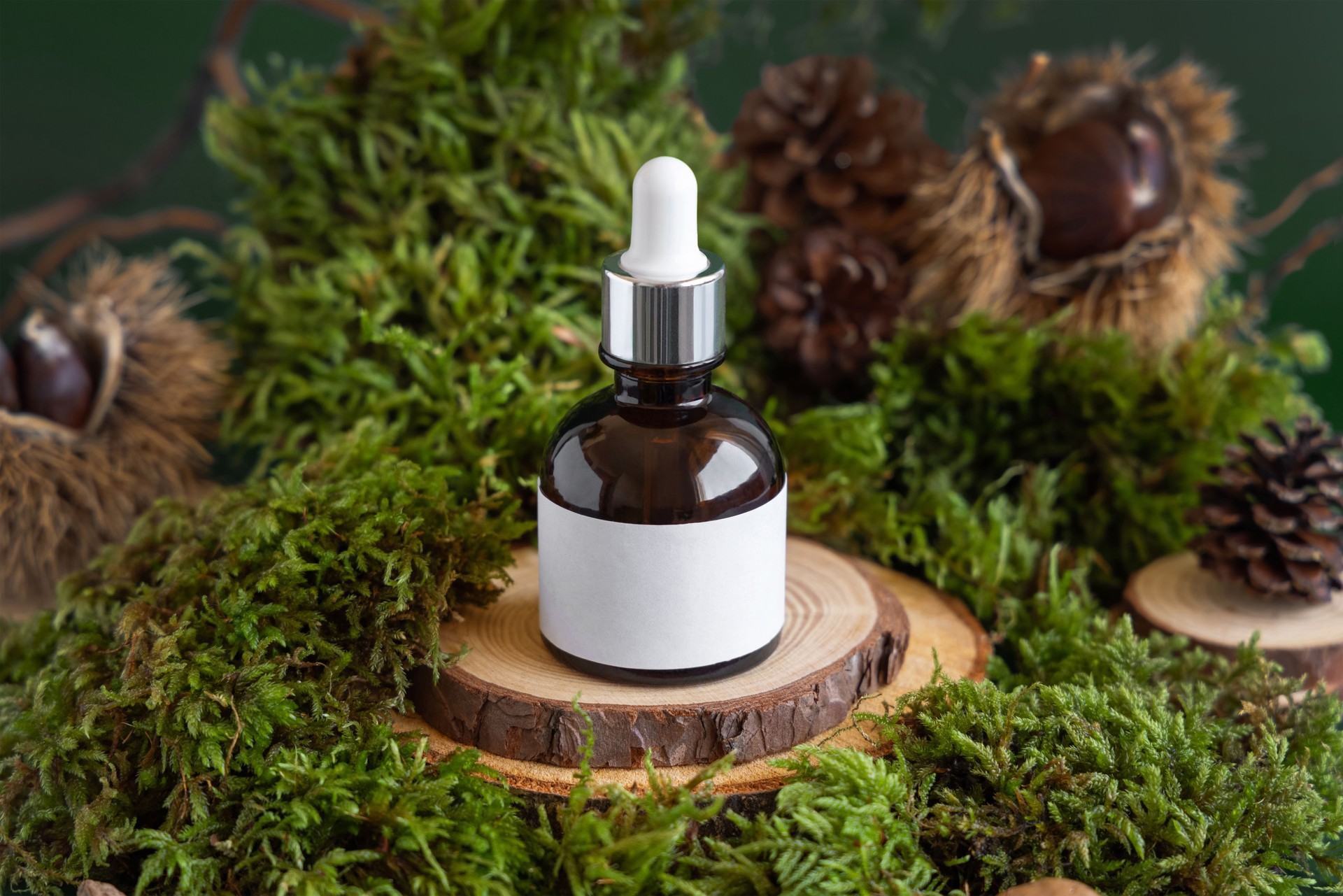 Glass dropper cosmetic bottle on wooden piece between green moss, close up. Label mockup